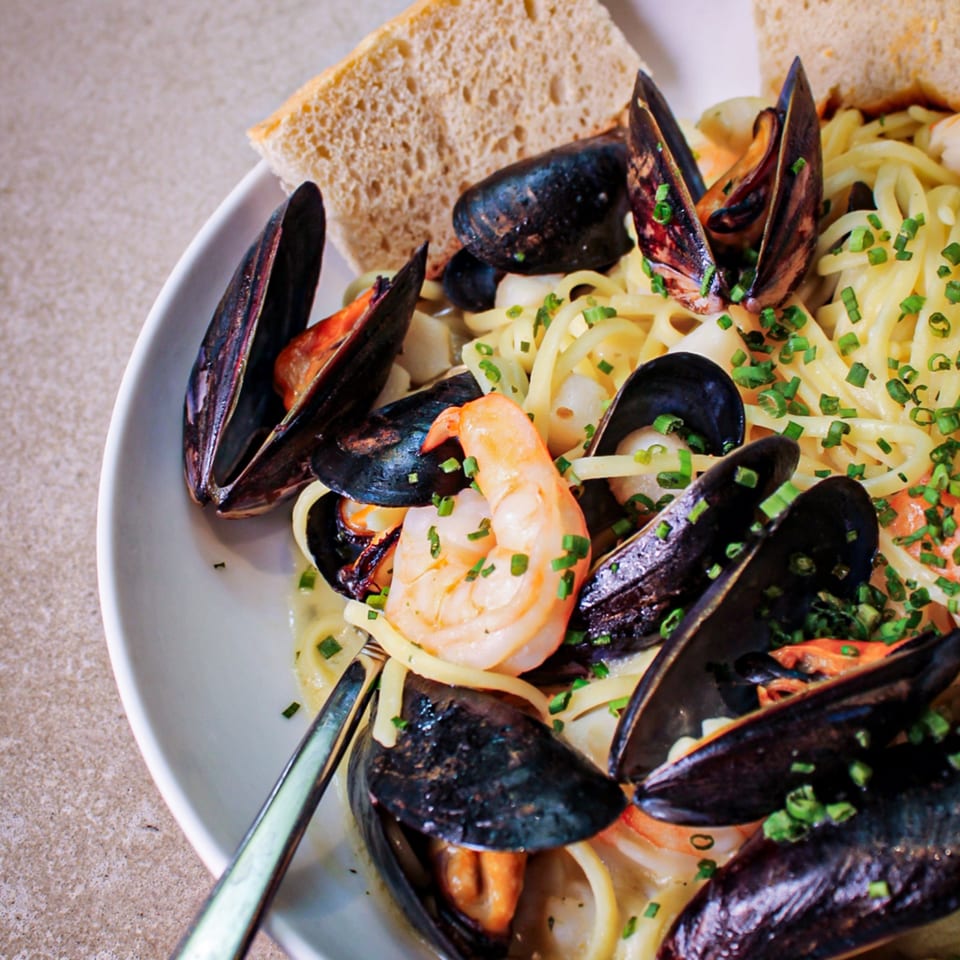 Seafood pasta with mussels and shrimp, garnished with chives and served with slices of bread.