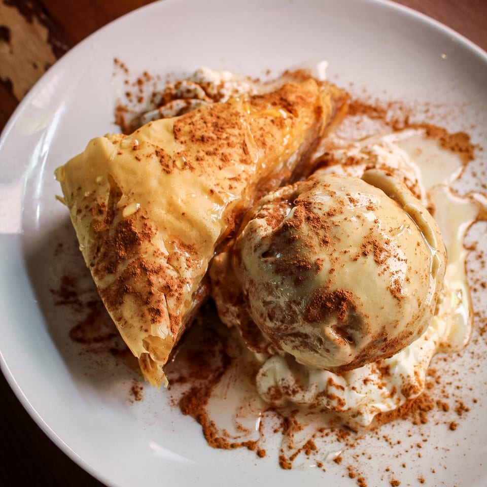 Golden flaky pastry served with vanilla ice cream, honey drizzle, and cinnamon on a white plate.