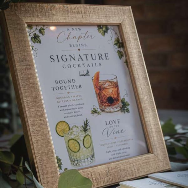 Framed restaurant sign displays illustrated signature cocktails, including a citrus-garnished drink, against a leafy outdoor setting.