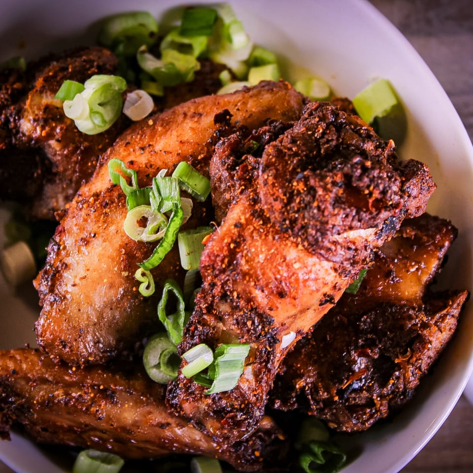 Plate of crispy spiced fried chicken garnished with sliced green onions and lime wedges.