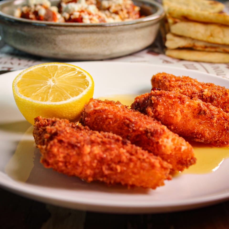 Crispy fried chicken pieces with a lemon half on a plate, alongside a bowl of salad and stacked flatbread.