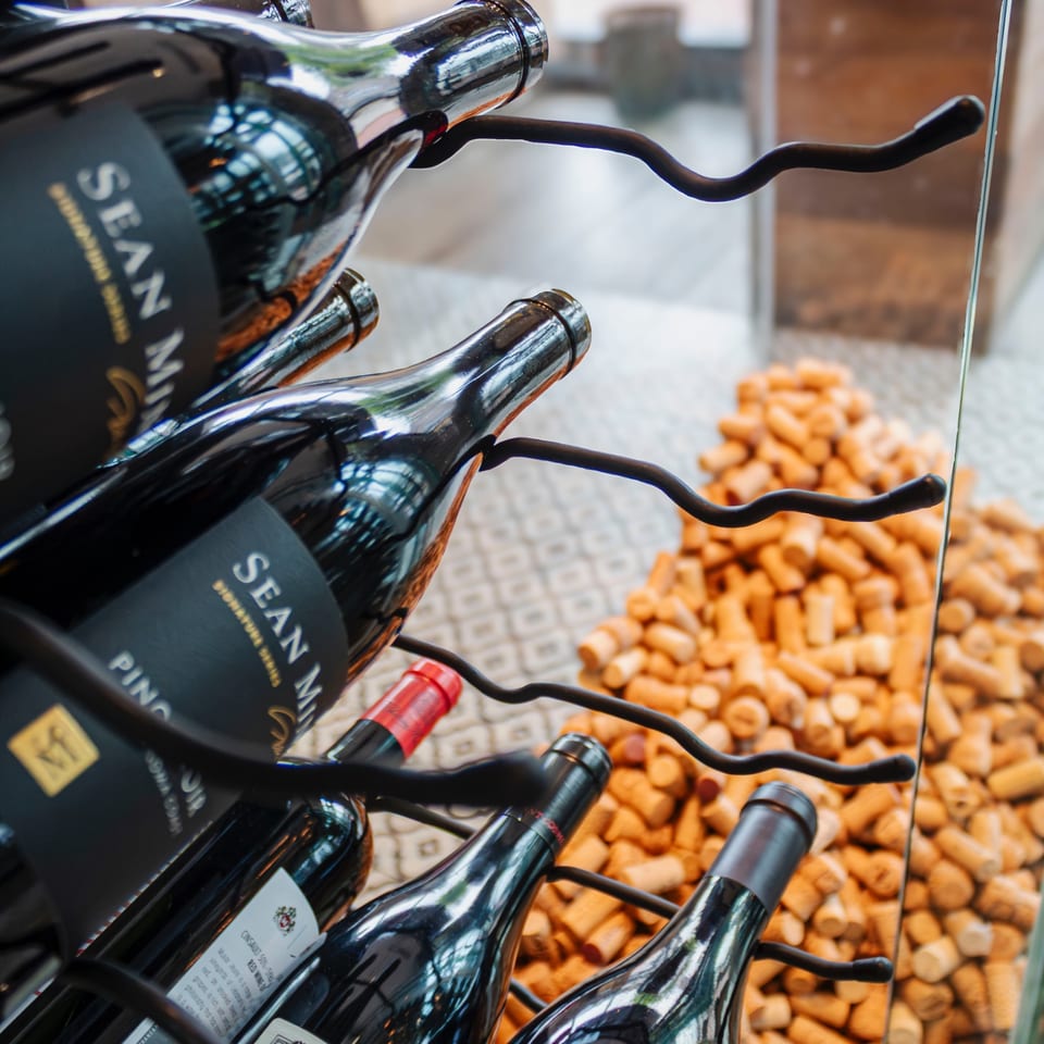Wine bottles displayed beside a bin filled with natural corks in a restaurant or wine shop.