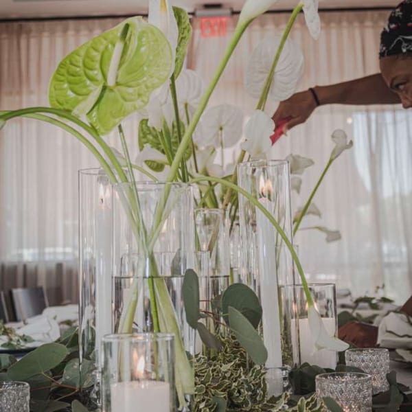 Lush white and green floral centerpiece with lit candles decorates a restaurant dining table as a person arranges flowers.