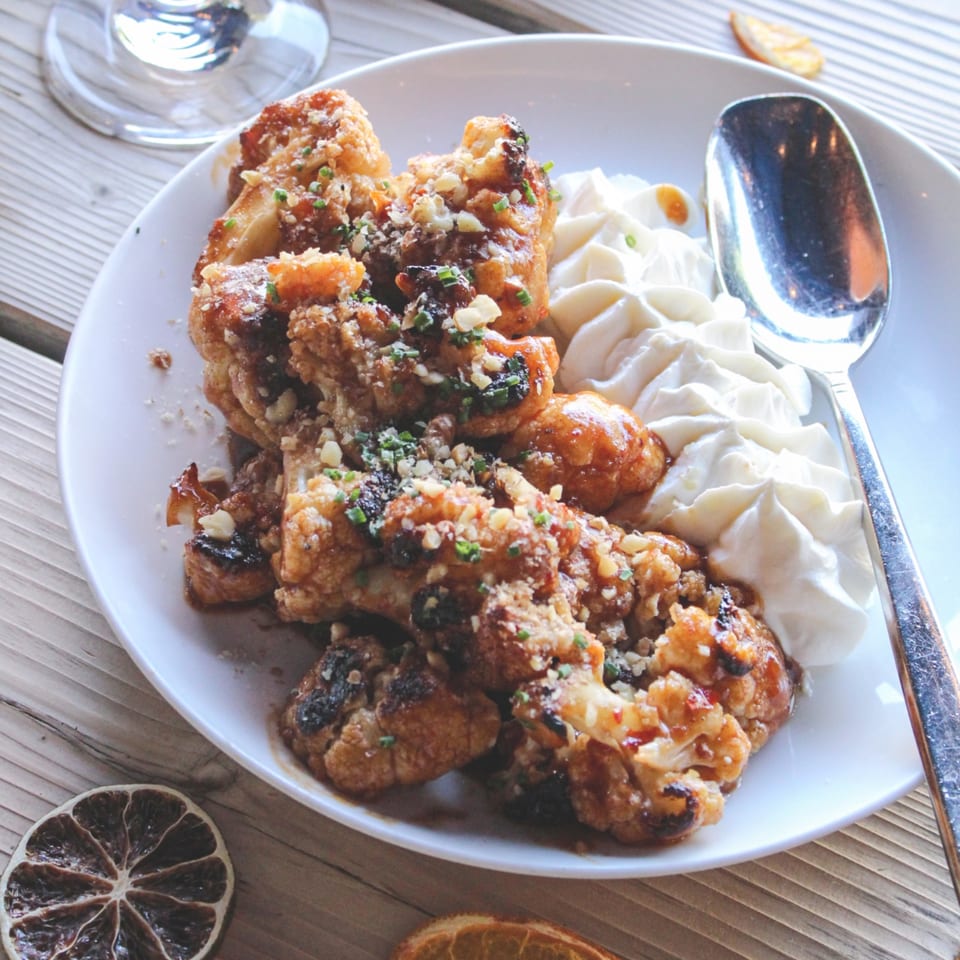 Plate of crispy roasted chicken pieces with mashed potatoes, herbs, and a spoon on a wooden table.
