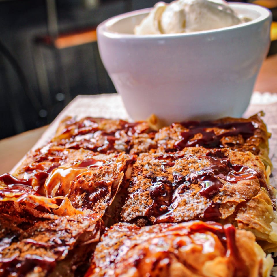 Glazed pastry dusted with powdered sugar and cinnamon, served on a plate with a bowl of vanilla ice cream.